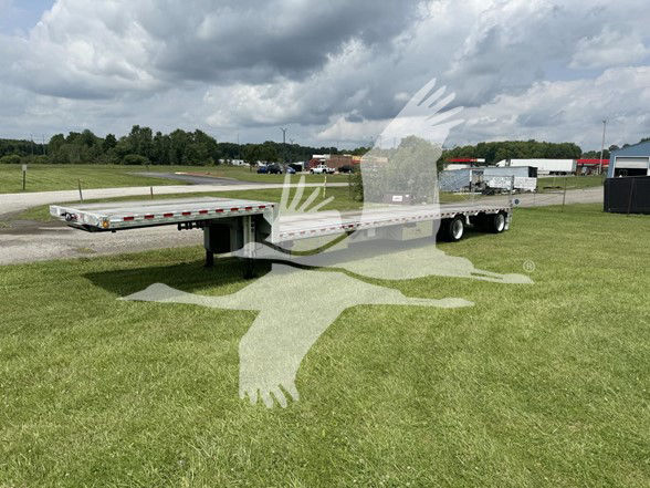 Trailer showcasing flatbed with drop deck expandable design, long metal frame, and wheels in field under cloudy sky.