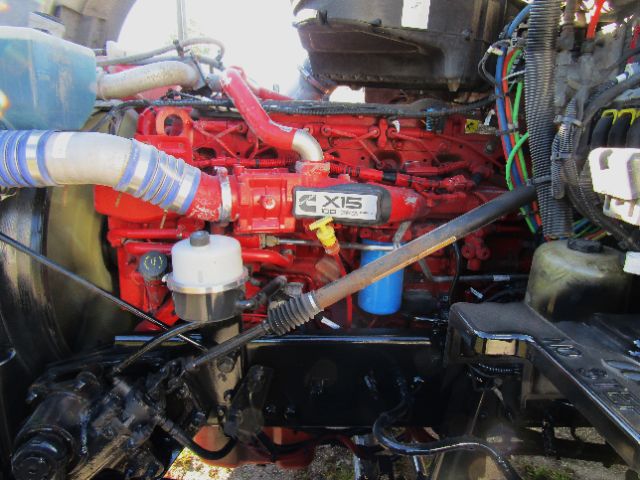 Kenworth T680 engine bay showing red inline engine with X15 badge, blue hoses, white brake reservoir, and various wiring harnesses.