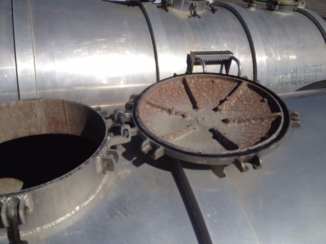 Open manhole cover on top of a metal vacuum tank with round access hatch and riveted seam.