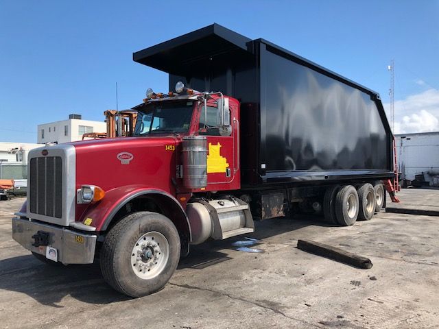 Peterbilt 388 dump truck with a black dump bed and red cab, side view parked on a lot.