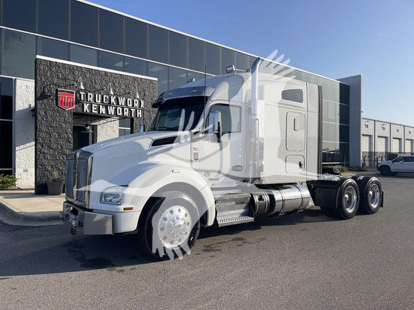 Kenworth T880 tractor in front of TruckWorks Kenworth dealership showing a white cab with sleeper area and three rear axles.