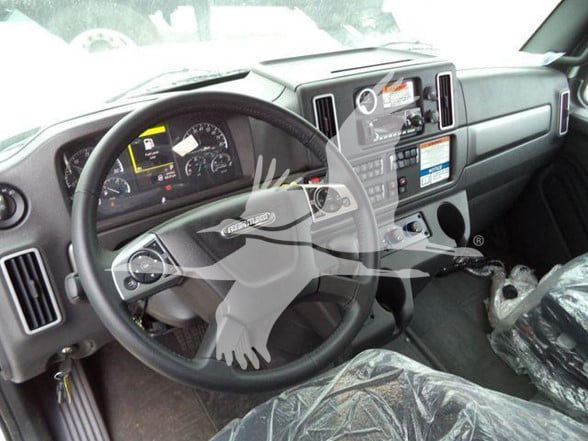 Freightliner truck interior showing steering wheel, dashboard, and control cluster. Center console with screens and gauges visible.