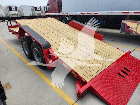 Trailer flatbed with wooden deck and red frame showing dual rear axles and ramps in a loading yard.