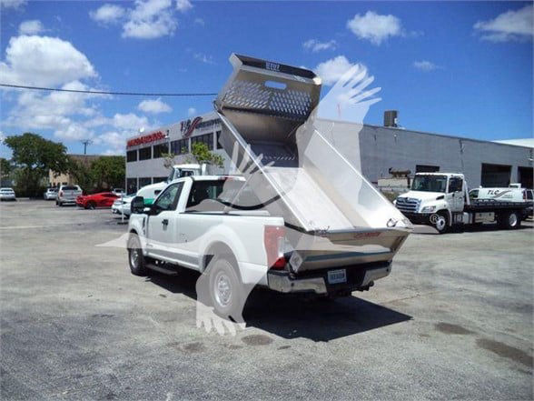 Truck body chassis with a large dump bed in raised position attached to a white pickup, showing aluminum rear tailgate and side panels.