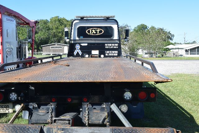 Peterbilt 337 truck cab in rear view on a flatbed rollback. Visible text on cab includes QXT logo and slogans. Tag or sticker on bumper area near taillights.