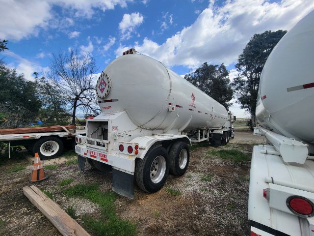 Tank trailer showing rear and side view with dual rear axles and hazard placard, white tanker, Freightliner Cascadia not visible.