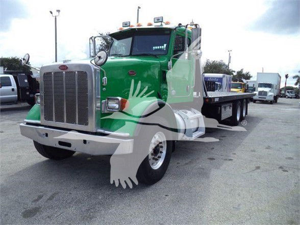 Peterbilt 367 tow truck front-left view with green cab and silver bumper, low-profile flatbed in rear.