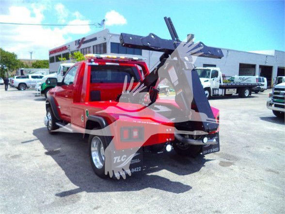 Tow truck with a hydraulic arm extended at rear; red body with black lifting mechanism and multiple trucks in background.