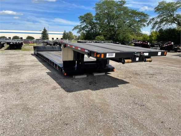 Fontaine Renegade 18 LX40 double drop deck trailer showing flatbed with black paint and wooden deck, in a gravel lot.