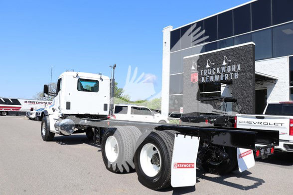Kenworth T880 cab and chassis truck in a dealership lot with white cab and dual rear axles, Kenworth branding on mud flaps.