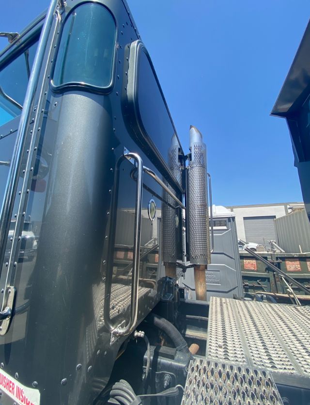 Peterbilt truck cab side with exhaust stacks and access ladder visible.