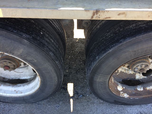 Two tandem trailer wheels with black tires and silver rims; dirt and rust visible on rims and drum hubs.