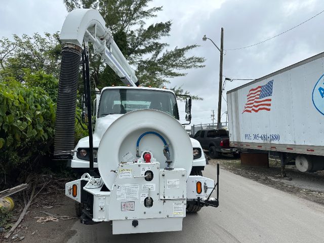 Front view of a 2014 Freightliner 114SD vacuum truck with a circular back panel, hose reel, and vacuum hose, parked on a narrow street.