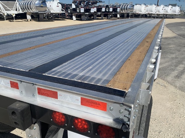 Flatbed trailer bed showing corrugated metal decking with wood inserts and rear lighting panel.