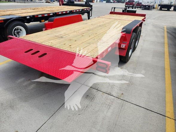 Flatbed trailer with wooden deck and red ramps. Behnke BT logo on fender; drill holes on ramp; dual axle with black tires.