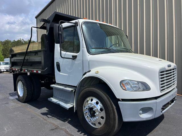 Freightliner M2 106 dump truck side profile showing white cab, black dump bed, and chrome wheels.