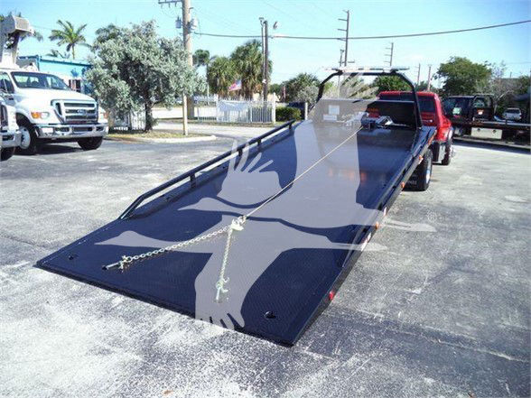 Ram 5500 tow truck bed with ramp and chains visible in a dealership lot.
