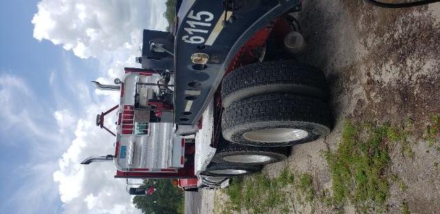 Kenworth TRIAXLE tractor-trailer in-service showing rear deck with tool boxes and triple rear axles, red cab, aluminum toolbox and black flatbed with white wheel wells.