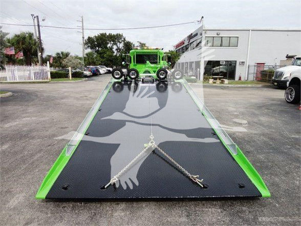 Tow truck transporter ramp with Peterbilt 337 listing text visible in the foreground: VIN and stock number not visible on ramp; image shows a green tow truck with a dark loading ramp and chains.