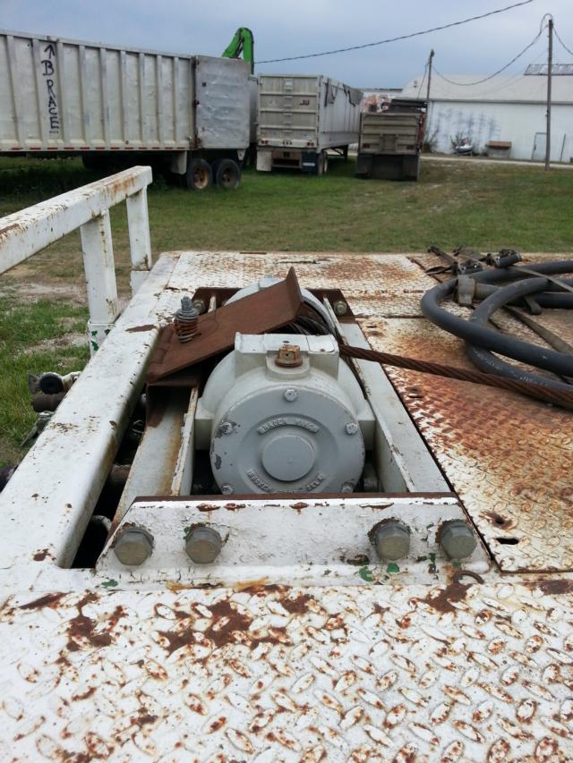 Trailers with rusted lowboy deck and a gray electric motor winch assembly mounted on a white, rust-streaked platform; cables and fittings present.