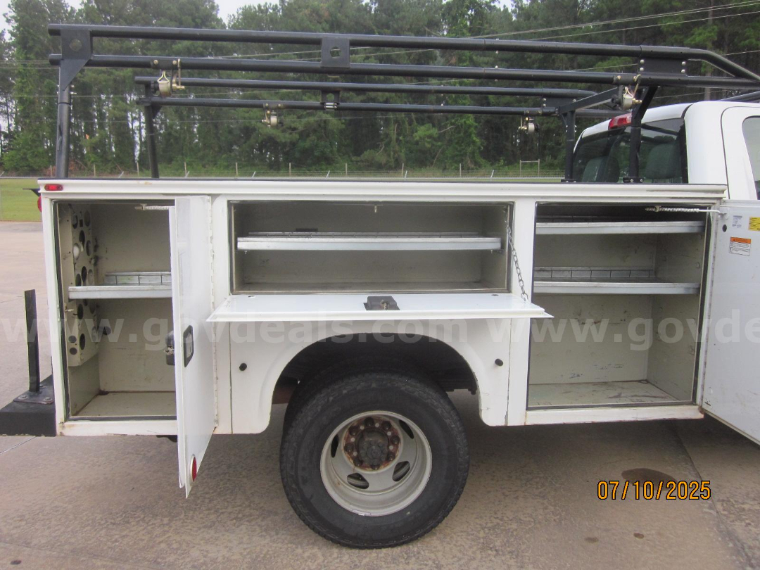 Truck utility service body side compartments open showing drawers and shelves with ladder rack above.
