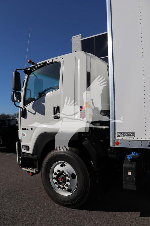 Isuzu FTR truck cab with box body. Visible text includes 'LONCOACH' on the side of the box and various truck details on the cab; front wheel and door area visible.