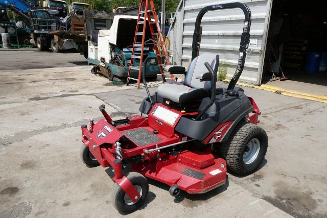 Red Ferris IS 700Z standing in a lot with seat, roll bar, and mower deck; black roll bar, grey seat, and large rear tires; surrounding equipment and buildings in background.