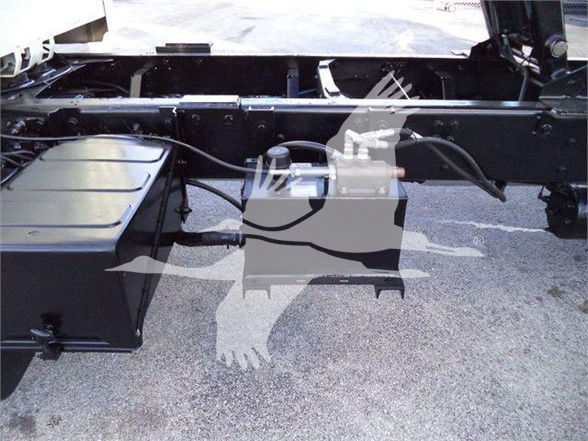 Truck chassis undercarriage view with fuel tank and hydraulic lines visible.