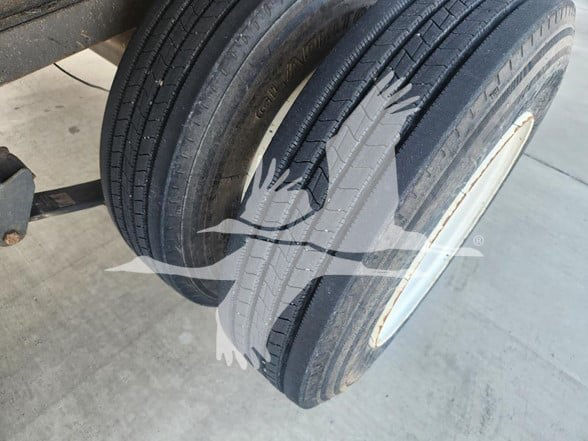 Trailer dual tires on a flatbed trailer showing tread and white wheel rim; watermark of a bird logo over image.