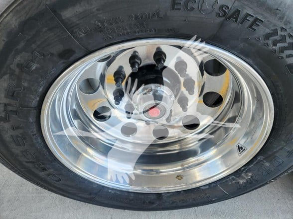 Trailer wheel showing polished aluminum rim and black tire with visible lug nuts and valve stem.