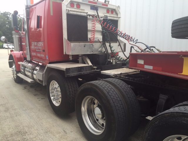 Truck cab side with red Western Star 4900fa sleeper, chrome fuel tanks, dual rear axles, coiled air hoses, and a flatbed trailer connection.