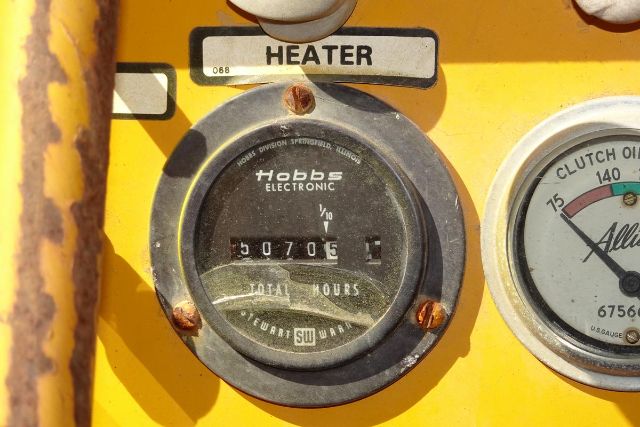 Grove RT58 crane dashboard with Hobbs electronic hour meter showing 30705 hours and a heater label above. Right gauge shows clutch oil pressure gauge with numbers. Rusty yellow panel.