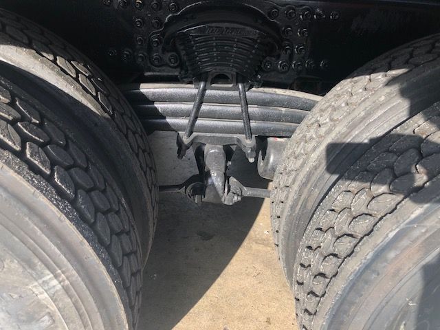 Rear view of Freightliner truck chassis showing tandem axle dual tires, suspension, and fifth-wheel/kingpin area in center.