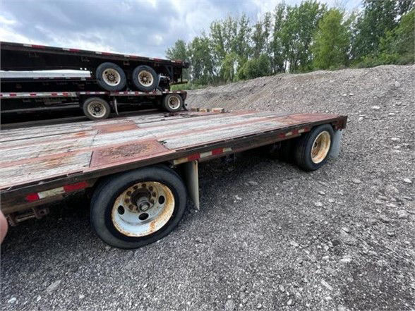 Dynaweld steel stepdeck trailer with dual axles and flatbed deck, showing rusted steel surface and white wheels.