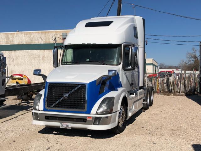 Volvo VNL64 conventional sleeper truck with white and blue paint, front grille, and side mirrors visible.