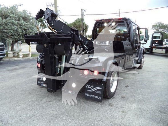 Tow truck rear view with hook lift mechanism and lighting; TLC logo on mudflaps; tail lights and rear bumper visible.