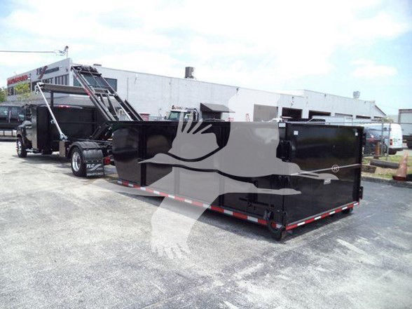 Flatbed trucks in a lot with a large black dump trailer attached. Chevrolet Silverado 6500HD badge not visible.