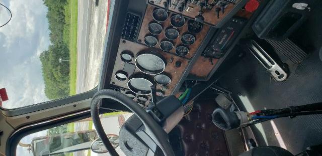 Truck cab dashboard with multiple gauges and steering wheel, Kenworth conventional daycab interior visible.