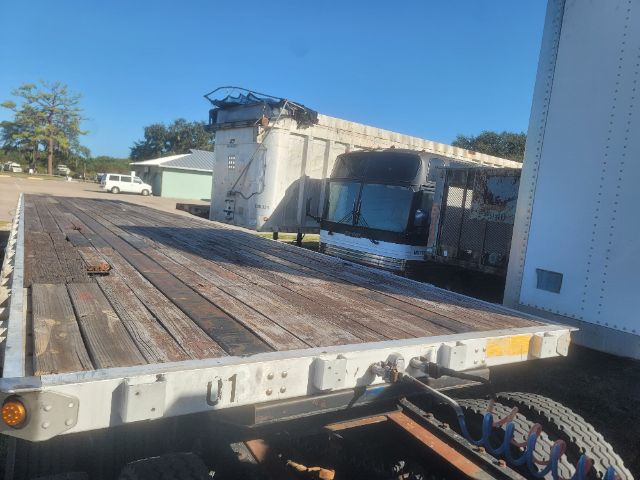 Utility flatbed trailer with wooden deck, gray steel frame, and U1 marking; cab of truck in background and clear blue sky.