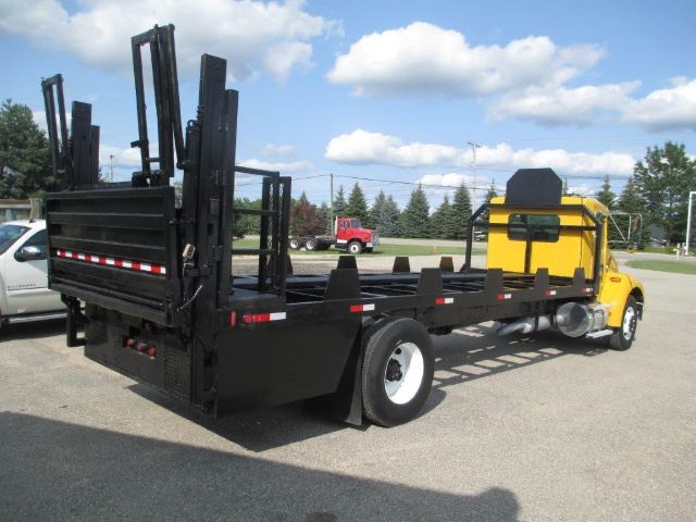 Flatbed tow truck with a yellow cab and black flatbed, loading ramps raised at rear, side rails and wheel wells visible.