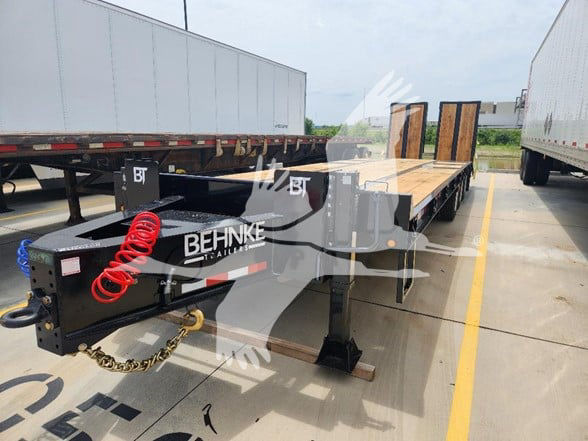Flatbed trailer tongue with Behnke branding and PTO/air hoses visible; long flatbed section with wooden deck and black frame.