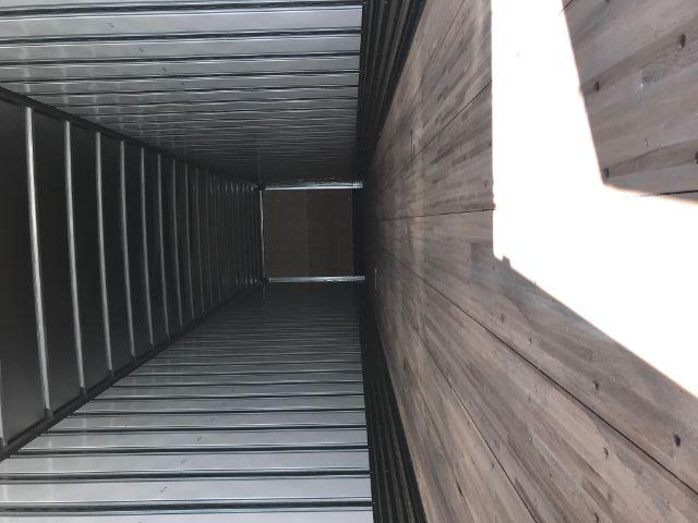 Interior of an empty metal trailer with wooden floor, long rectangular cargo space, door at far end.