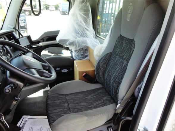 Truck cab interior showing driver's seat and steering wheel with plastic seat covering and a cardboard box in the background.