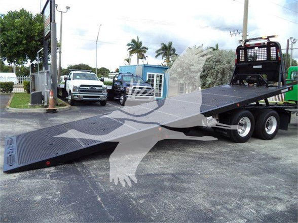 2014 Peterbilt 367 tow truck with a long flatbed in a parking lot, dual rear wheels, and a raised loading platform.