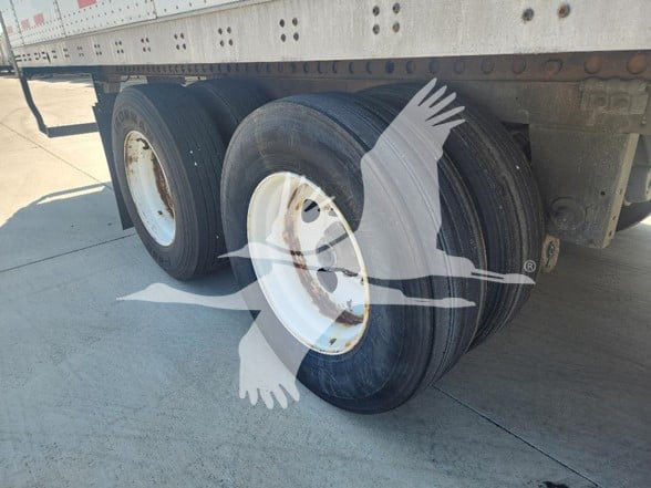 Trailer rear dual axle with black tires and white rims under a metal cargo trailer.