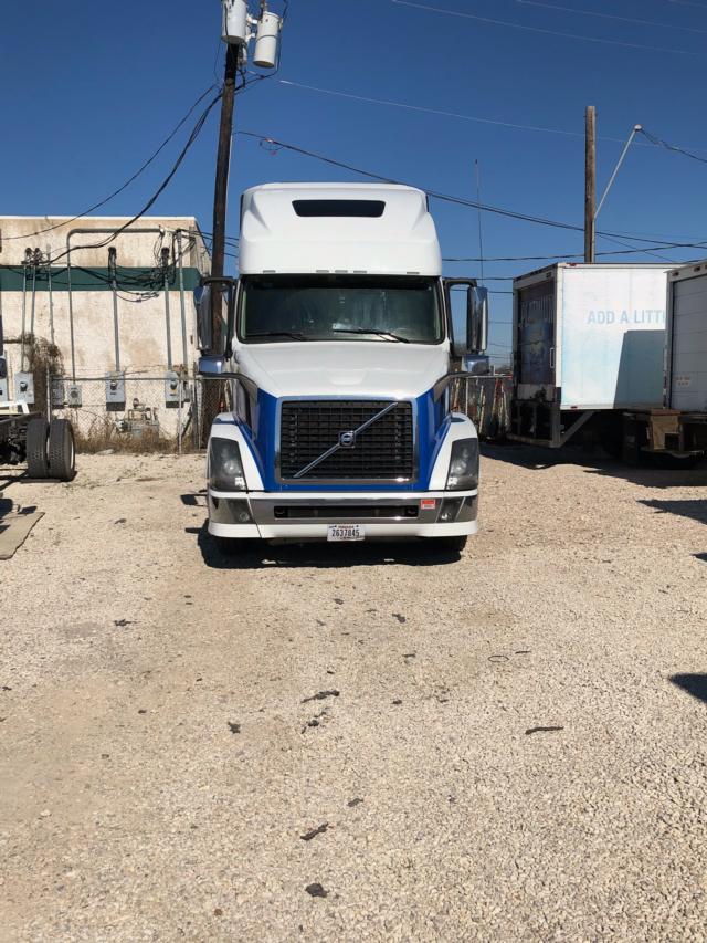 Front view of a white Volvo VNL64 truck with blue grille accents, cab-over design, and a license plate on the front bumper.