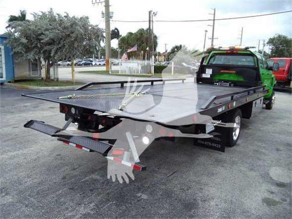 Tow truck with a flatbed loaded on a green International CV truck. Visible text includes 3/4 view of bed and ramps; no legible serials or logos clearly readable on components.