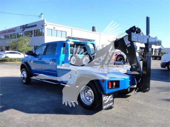 Blue 2023 Ram 5500 tow truck with a crane/boom on the back. Visible text includes dealership signage and stock number in the background.