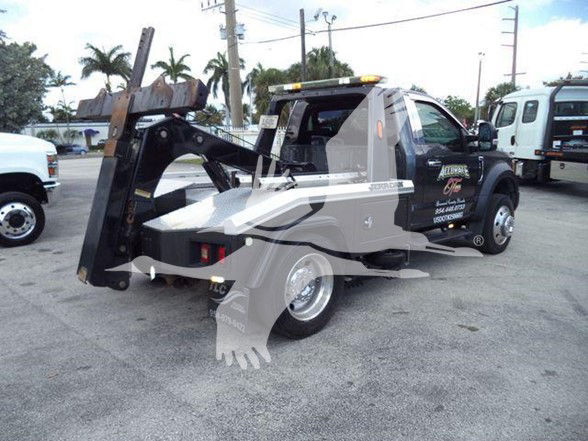 Tow truck with a hydraulic tilt bed, black cab, and gray bed. Visible text on side likely includes company branding.