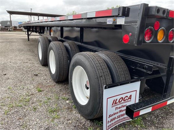 Flatbed trailer with three axles and extendable deck; rear taillights and safety reflectors visible; black frame with white wheels; LLOCA sign on mudflap.